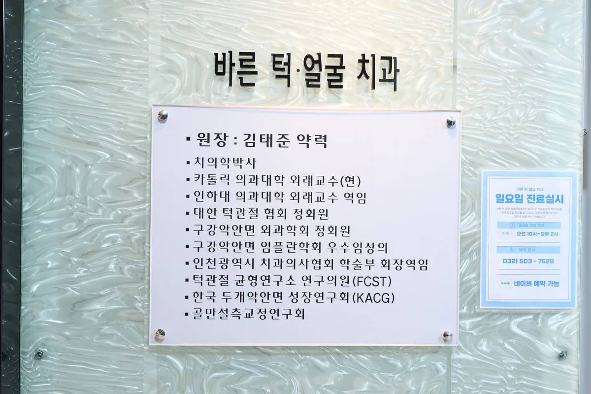 바른턱얼굴치과의원 입구 유리벽 — ‘바른 턱·얼굴 치과’ 글자와 대표원장 약력 명판, 일요일 진료 안내